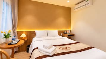 Una habitación de hotel con una cama, una mesita de noche, una lámpara, una pequeña mesa con un jarrón de flores y un equipo de aire acondicionado.