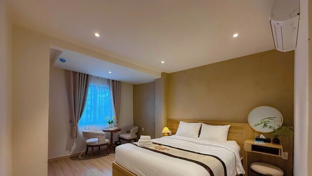 Une chambre d’hôtel avec un grand lit, des tables de chevet, un bureau, des chaises, une lampe et une fenêtre avec des rideaux.