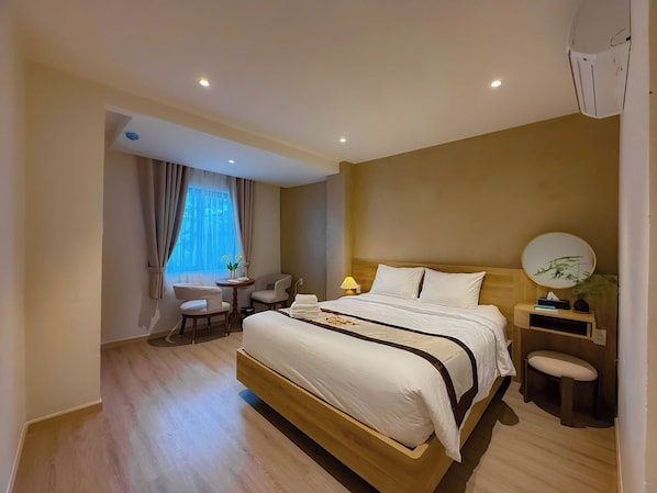 A hotel room with a large bed, bedside tables, a desk, chairs, a lamp, and a window with curtains. - Chinchu Stay (Thu Duc)