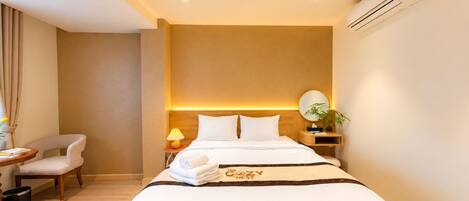 Quarto de hotel com cama, mesa de cabeceira, luminária, cadeira e unidade de ar condicionado.