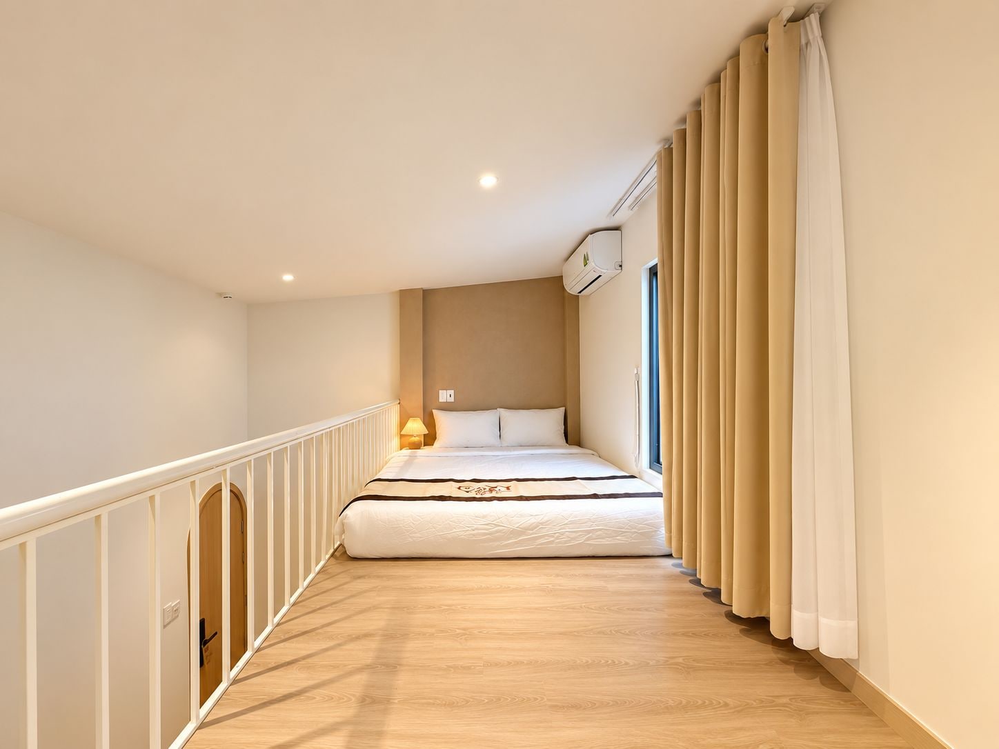 Habitación de hotel estrecha con cama, lámpara de noche y ventana con cortinas.