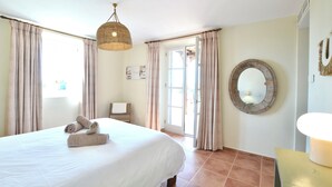 Une chambre d’hôtel avec un lit, des rideaux, un luminaire suspendu, un miroir et une porte donnant sur l’extérieur.