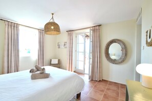 Une chambre d’hôtel avec un lit, des rideaux, un luminaire suspendu, un miroir et une porte donnant sur l’extérieur.