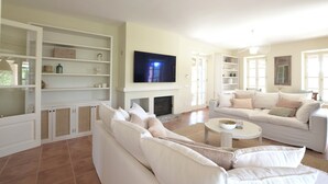 Ein geräumiges Wohnzimmer mit einem großen Flachbildfernseher, weißen Sofas und integrierten Regalen.