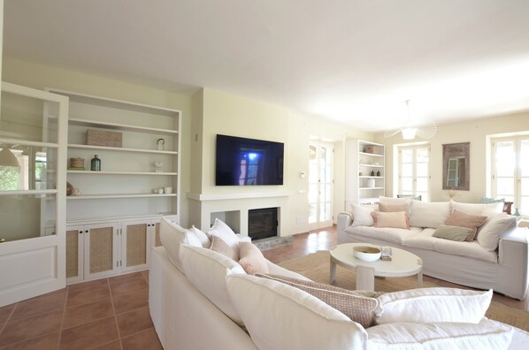 A spacious living room with a large flat-screen TV, white sofas, and built-in shelves.