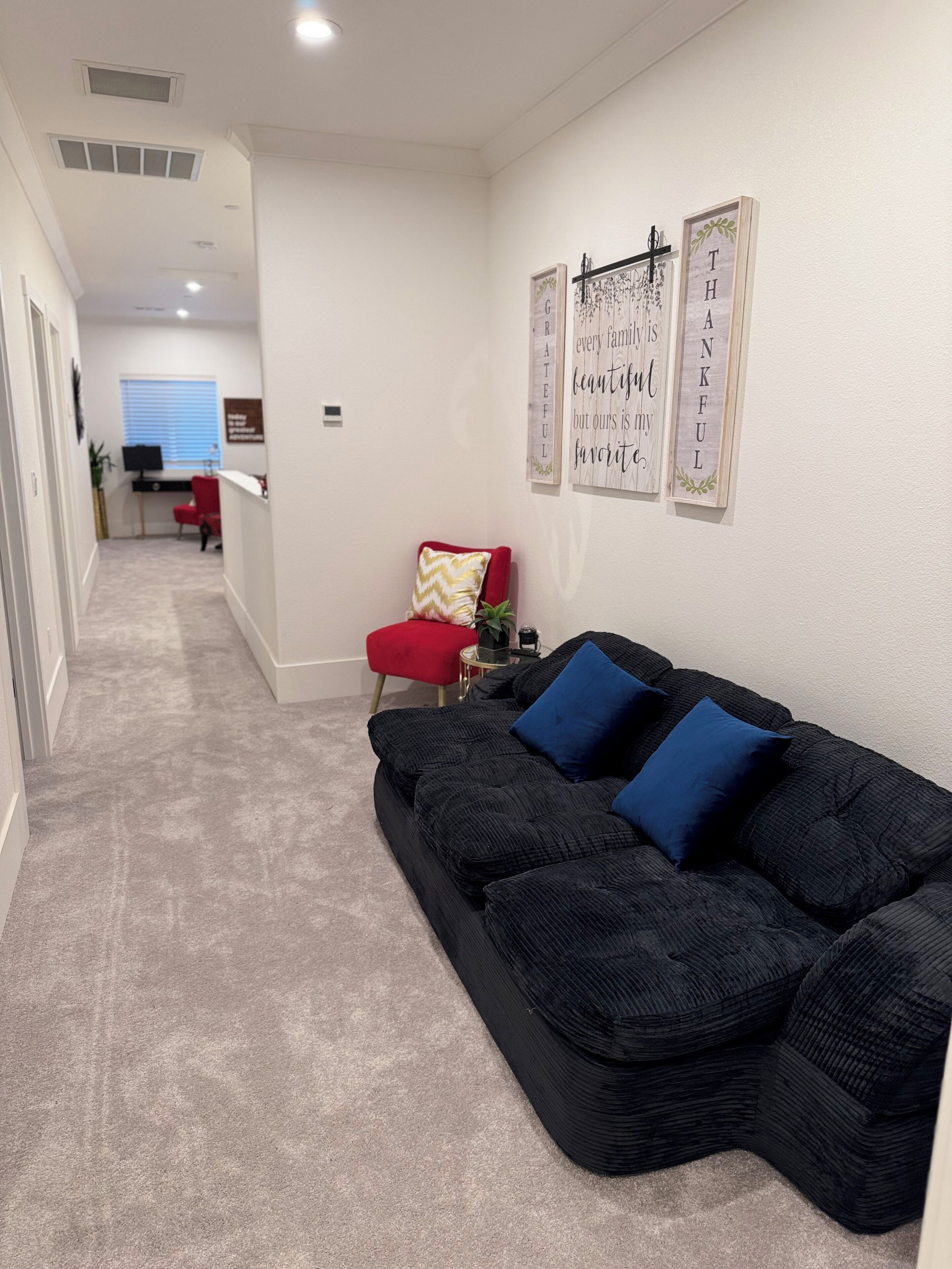 A living room with a black sofa, red chair, and two wall decorations.