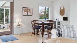 A dining area with a table and chairs, a lamp, a painting, and a view through a window. - 5 Star Holiday Home in Gedser (Gedser)