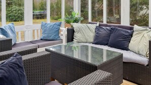 A covered outdoor seating area with wicker furniture and cushions, large windows, and a view of trees. - 5 Star Holiday Home in Gedser (Gedser)