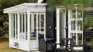 A conservatory with a glass enclosure, a black heater, and a bench outside a wooden house. - 5 Star Holiday Home in Gedser (Gedser)