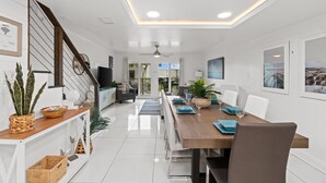 A modern, well-lit dining area with a wooden table, white chairs, and a staircase on the left. - Gorgeous Updated Condo steps from beach - Unit A14 (Panama City Beach)