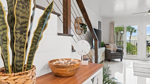 A modern living room with a wooden coffee table, a woven plant stand, and a view of the outdoors through large sliding glass doors. - Gorgeous Updated Condo steps from beach - Unit A14 (Panama City Beach)