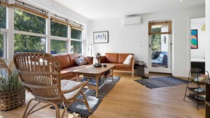 A spacious living room with a large window, a brown leather sofa, a wicker chair, and a wooden coffee table. - 5 Star Holiday Home in Sjaellands Odde (Sjællands Odde)