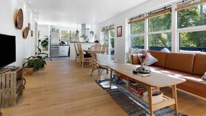 A spacious living area with a wooden floor, a dining table, a sofa, and large windows offering a view of greenery. - 5 Star Holiday Home in Sjaellands Odde (Sjællands Odde)