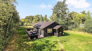 A small cabin with a deck, surrounded by trees and a grassy area. - 5 Star Holiday Home in Sjaellands Odde (Sjællands Odde)