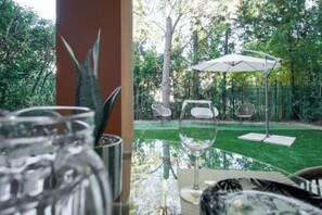 Una mesa de vidrio con sillas y un paraguas blanco en un jardín.