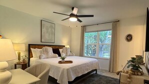 A hotel room with a bed, a desk, a chair, a ceiling fan, a window with curtains, and a television. - Near Watts Bar | Pet-Friendly | 2 Kings | Easy Checkout (Rockwood)