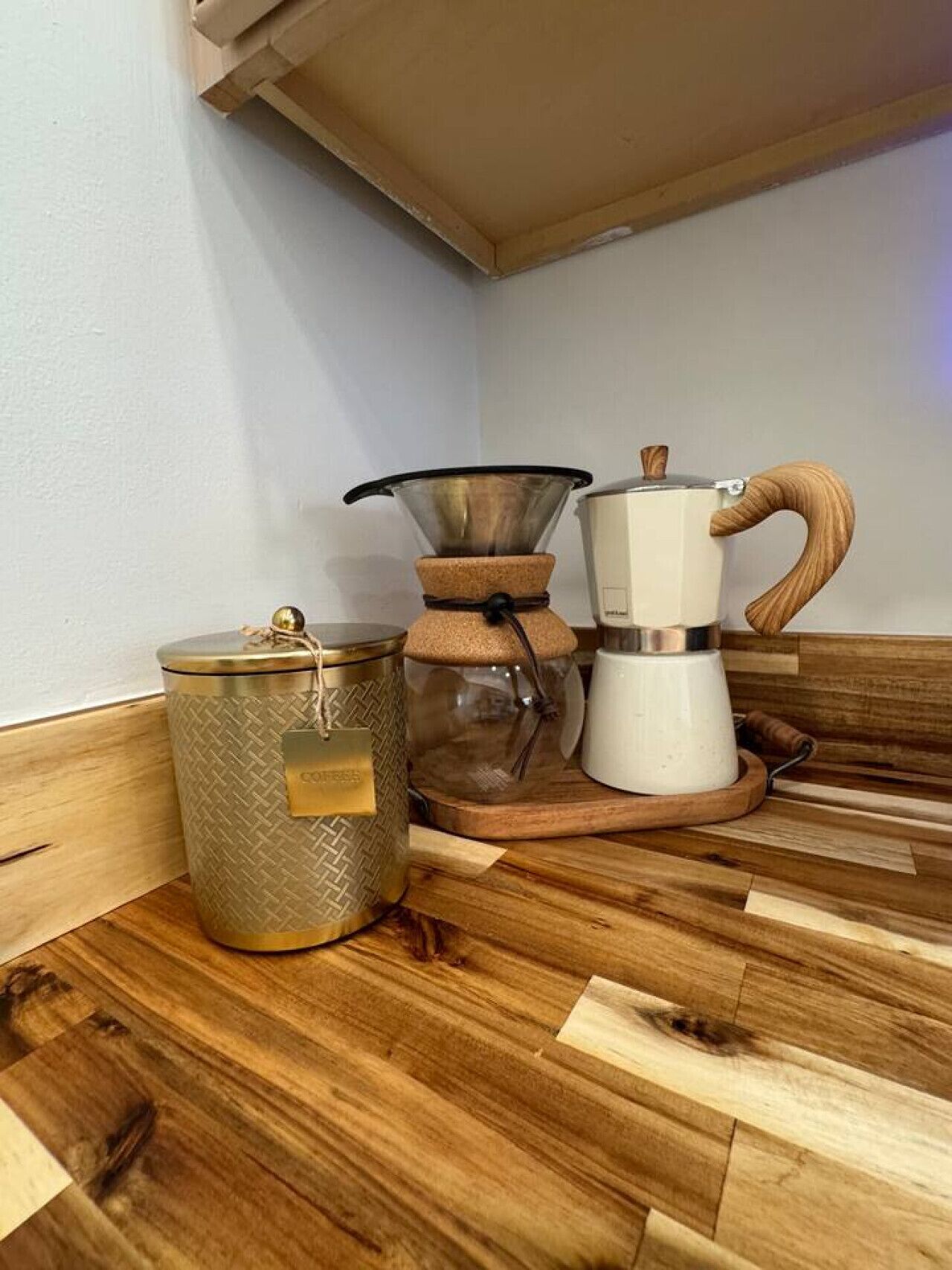 En kaffemaskine, et glas og en metalkande på en træoverflade.