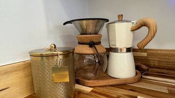 En kaffemaskine, et glas og en metalkande på en træoverflade.