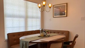 A dining area with a round table, brown upholstered bench, and four wooden chairs. A chandelier hangs above the table, and a framed picture is on the wall. - Near Watts Bar | Pet-Friendly | 2 Kings | Easy Checkout (Rockwood)