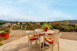 Un patio al aire libre con una mesa redonda y cuatro sillas, rodeado de plantas en macetas y vistas a una zona residencial.