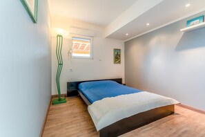 Un dormitorio con cama, lámpara de pie, ventana con persianas y estante en la pared.