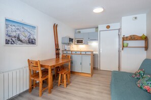 A compact living space with a wooden dining table, chairs, a kitchenette, a sofa, and a ski rack. - Studio at Alpe D'Huez with Mountain View, Balcony, and Wi-Fi for 3-4 Guests (Oz en Oisan Station)