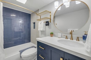A modern bathroom with a bathtub, toilet, vanity with a sink, and a large mirror.