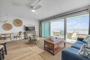 A spacious living area with a large window, a ceiling fan, and a wooden coffee table.
