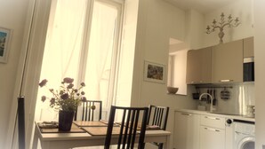 A kitchen with a washing machine, a dining table with chairs, a potted plant, and a window with curtains.