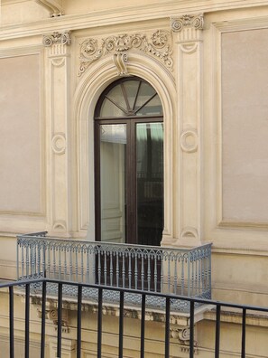 A building facade with an ornate arched window, a balcony with a metal railing, and classical architectural details.