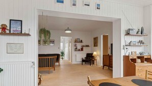 A spacious living area with a wooden floor, a dining table with chairs, a sofa, and a television. There are shelves with decorative items and a hanging plant. - 5 Star Holiday Home in Skagen (Skagen)