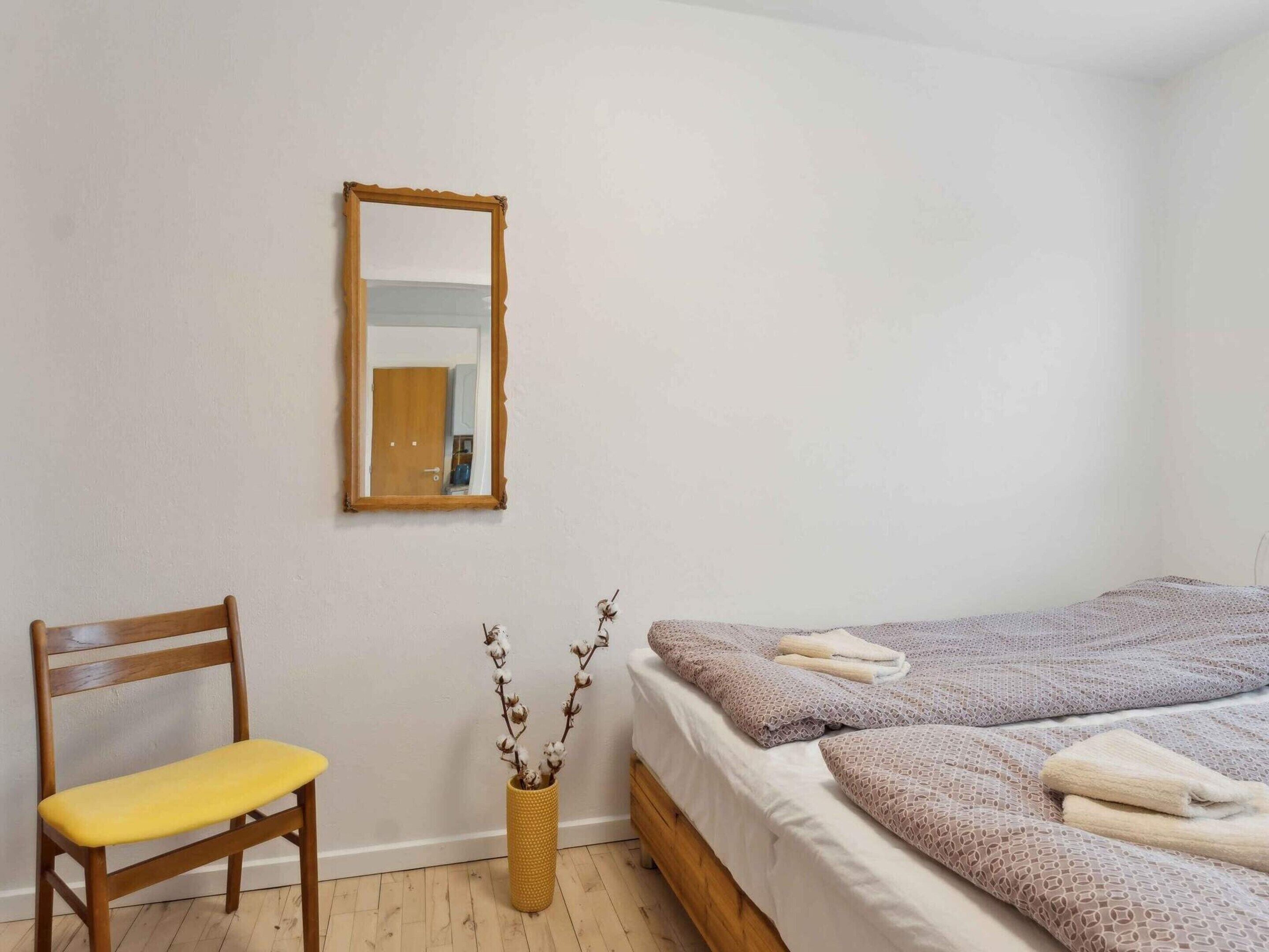 Ein Schlafzimmer mit einem Holzhocker, einem Bett mit Handtüchern, einem Spiegel und einer Vase mit Zweigen.