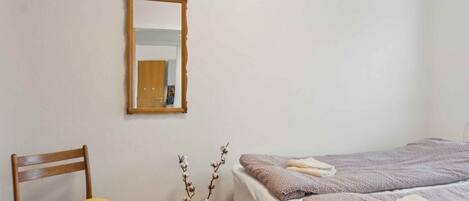Ein Schlafzimmer mit einem Holzhocker, einem Bett mit Handtüchern, einem Spiegel und einer Vase mit Zweigen.