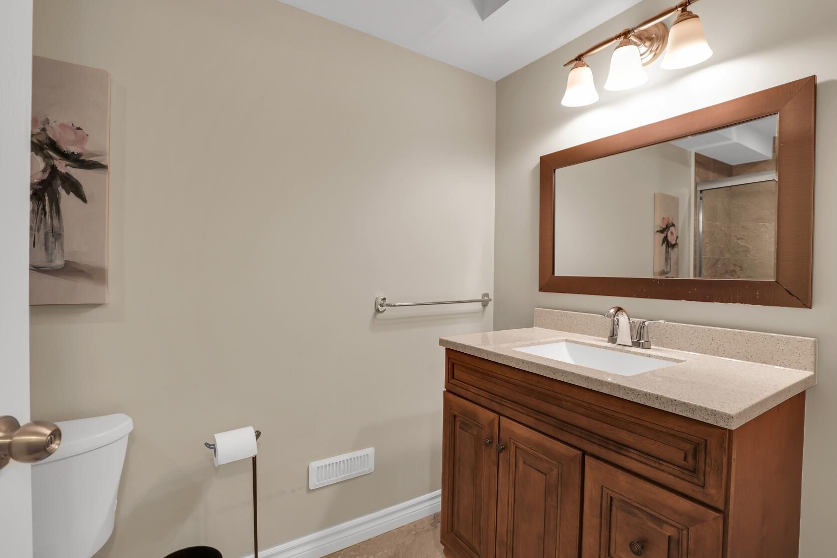 A bathroom with a beige wall, a wooden vanity with a sink, a mirror, and a towel rack.