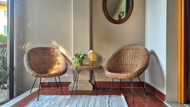 A balcony with two wicker chairs, a small table with a plant, and a mirror on the wall. - Casa di Amelie By Case al Lago (Sirmione)