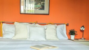 A bed with white bedding, a book on it, and a potted plant beside a bedside table with a lamp. - Casa di Amelie By Case al Lago (Sirmione)