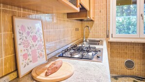 A kitchen with wooden cabinets, a gas stove, a sink, and a window with a view of greenery. - Casa di Amelie By Case al Lago (Sirmione)