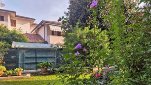 A garden with various plants and flowers, a fence, and a building with a tiled roof in the background. - Casa di Amelie By Case al Lago (Sirmione)