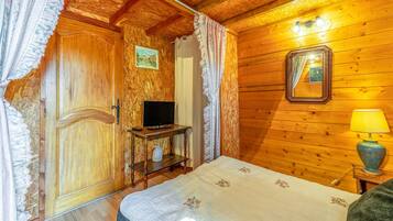A wooden room with a bed, a television on a stand, a lamp, and a mirror on the wall.