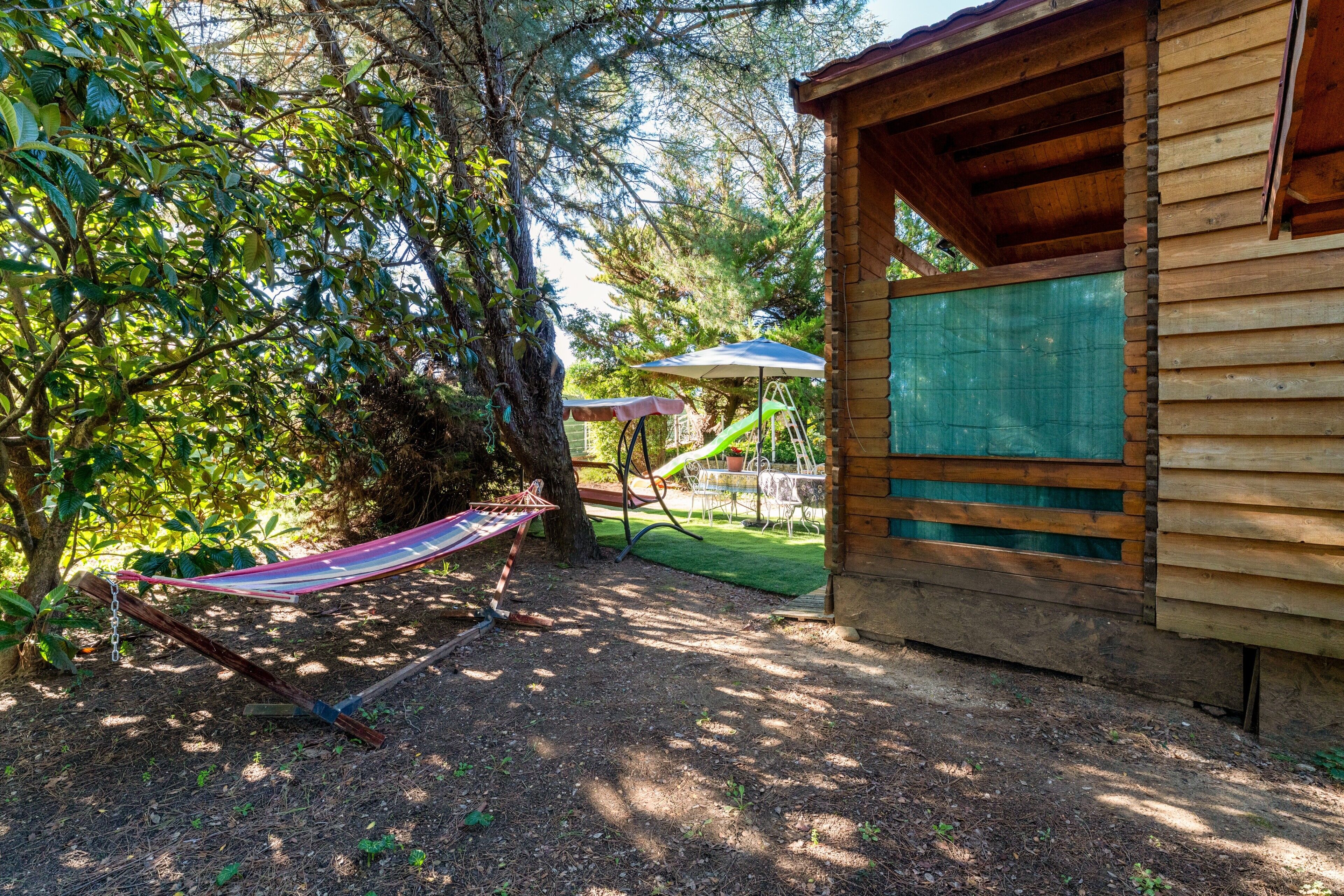 A wooden cabin with a hammock, a slide, and a covered seating area.