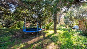 Un trampoline installé dans un espace boisé, avec des arbres et une petite construction en arrière-plan.