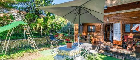 Une cabane en bois dotée d’un patio comprenant une table, des chaises et un grand parasol.