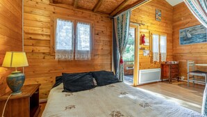 A wooden cabin room with a bed, a lamp, a chair, and a painting on the wall. - Chalet "Gîte" with Private Pool, Wi-Fi, and Air Conditioning (St Paulet de Caisson)
