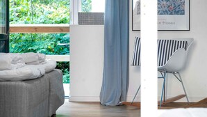 A bedroom with a bed, a window with a view of greenery, a blue curtain, and a chair. - 5 Star Holiday Home in Svaneke (Svaneke)