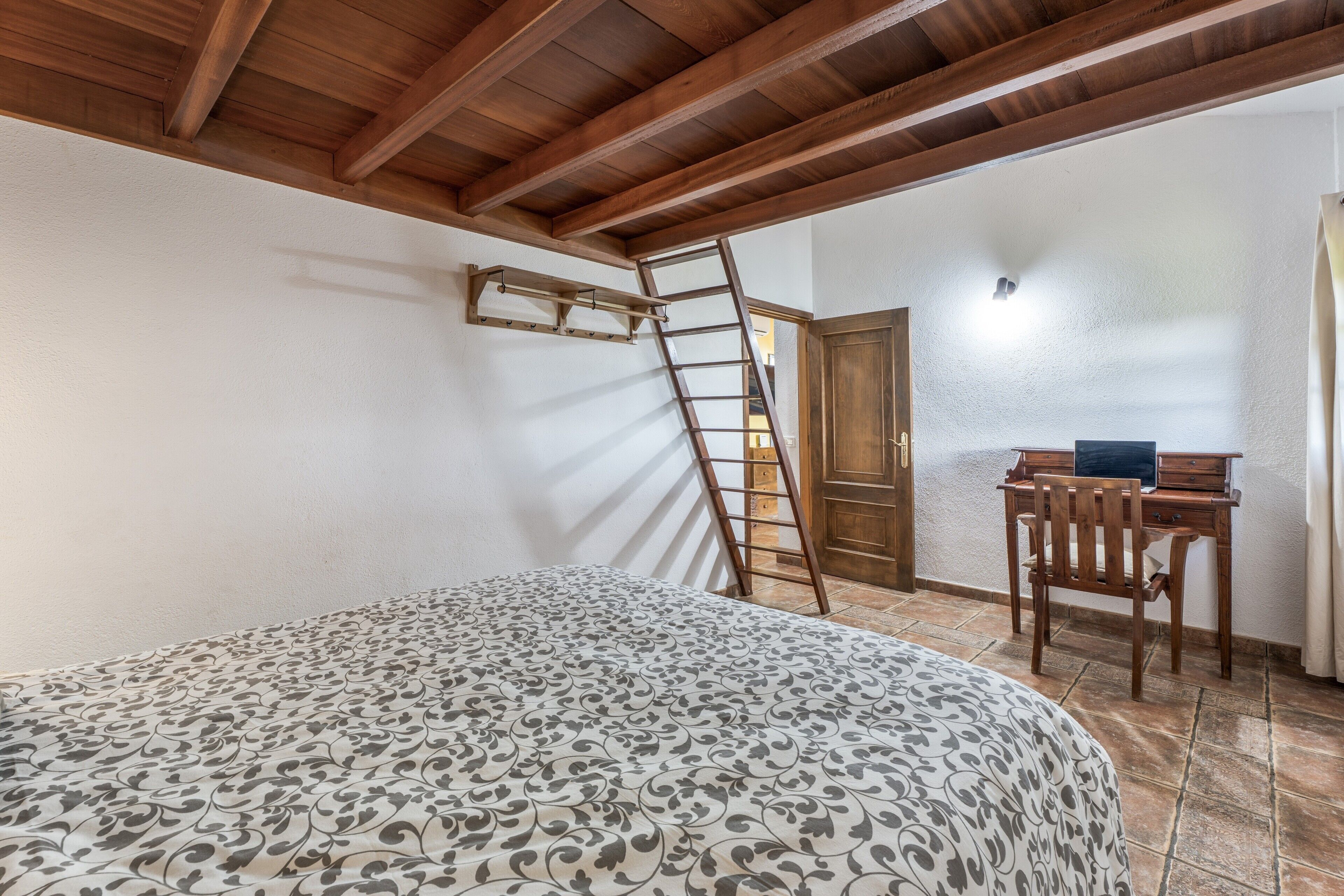 Un dormitorio con cama, escritorio de madera, escalera y puerta.