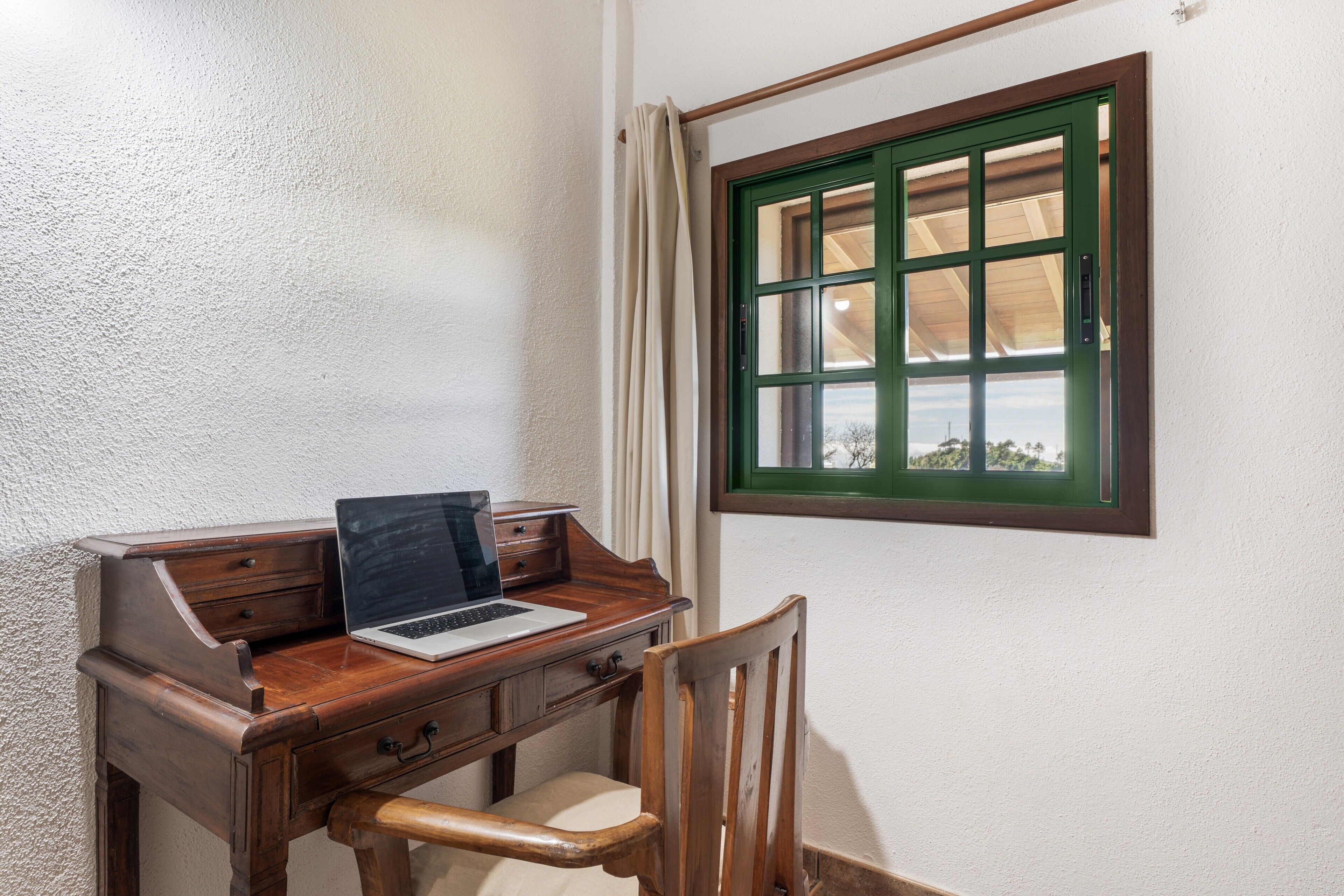 Ein Holztisch mit einem Laptop, einem Stuhl und einem Fenster mit grünem Rahmen.