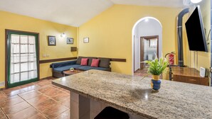 Una sala de estar con un sofá, una mesa de centro, una zona de cocina con un fregadero y una puerta que da a otra habitación.