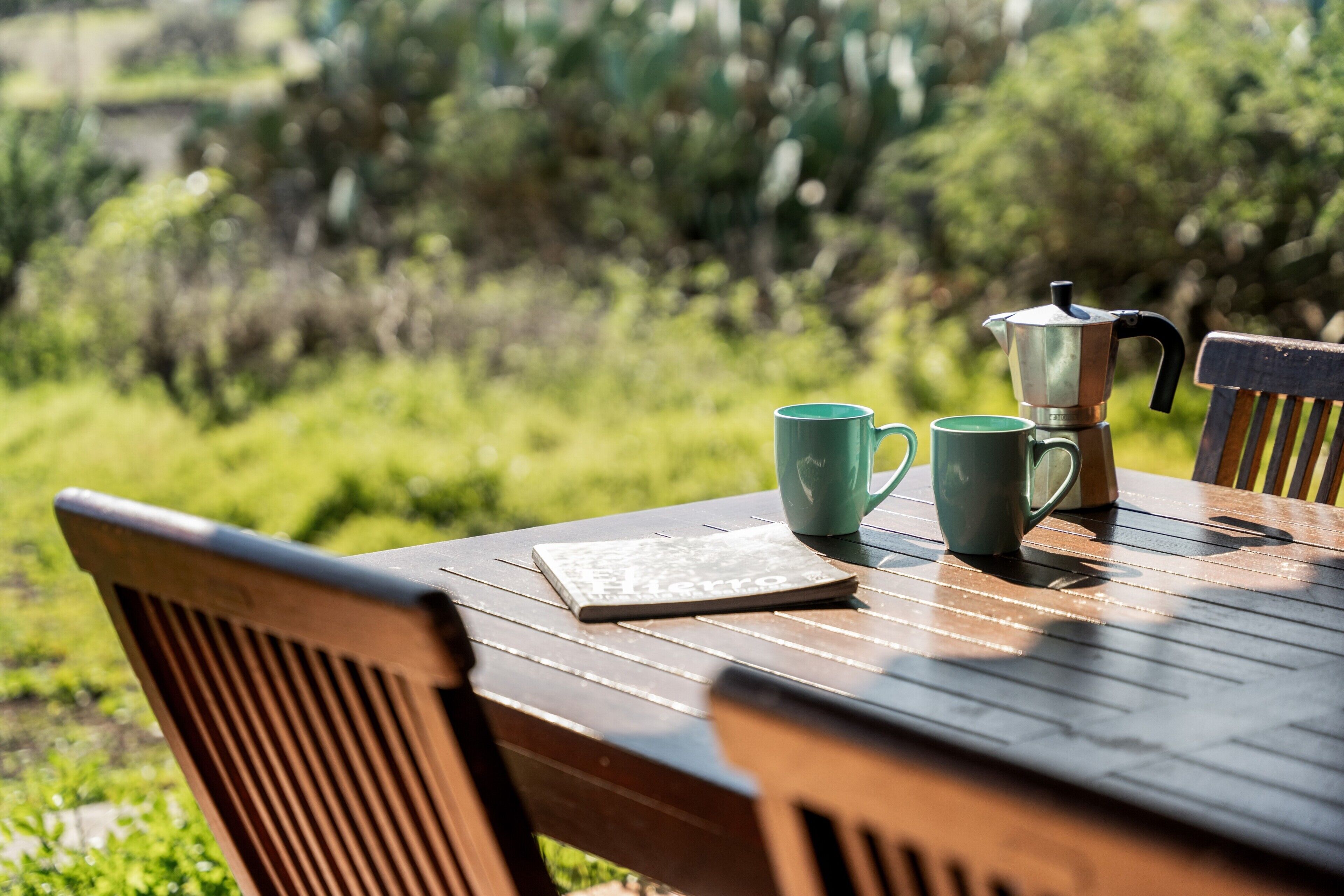 Una mesa de madera con una libreta, dos tazas verdes y una cafetera.