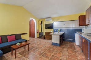 A compact living space with a sofa, a small table, a kitchen area with a microwave, and a tiled floor.