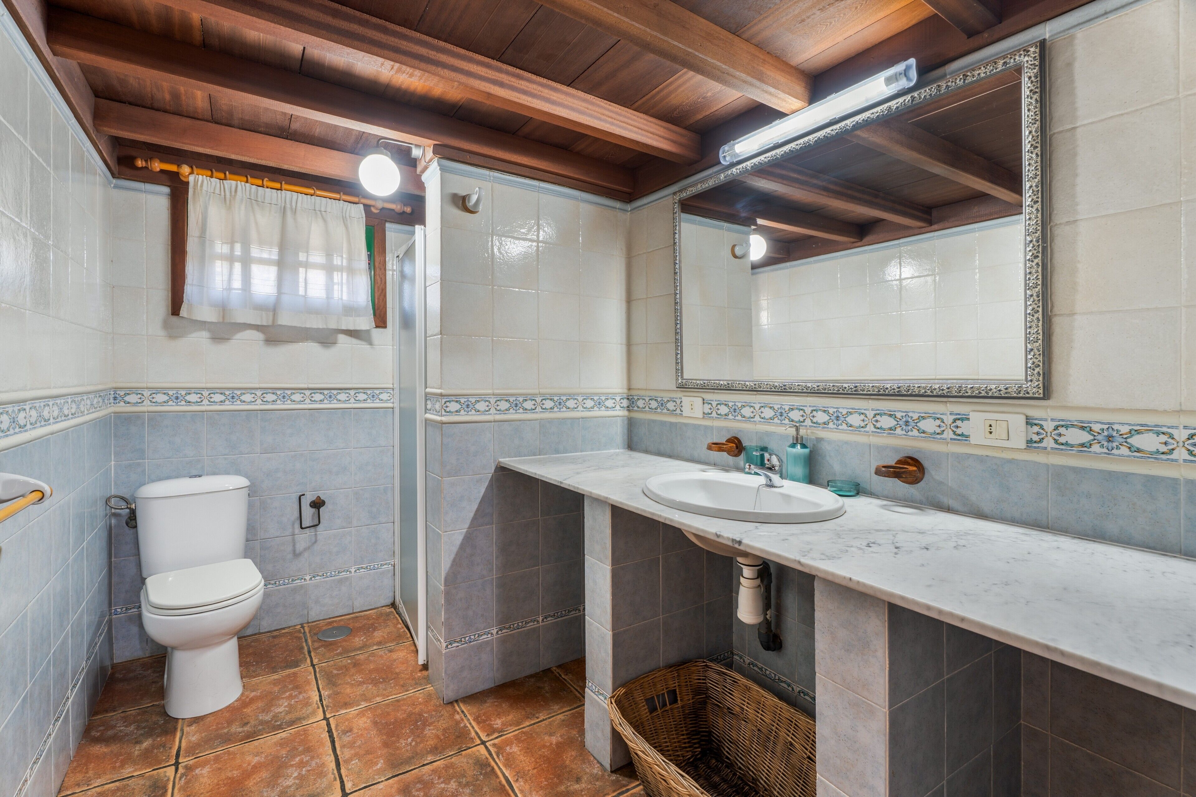 A bathroom with a toilet, sink, mirror, and tiled walls.